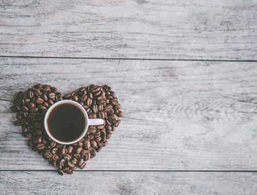 coffee filled white ceramic mug beside brown coffee beans on beige wooden surface