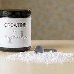 a bottle of creatine next to a spoon on a table