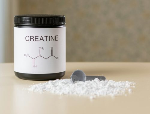 a bottle of creatine next to a spoon on a table