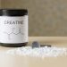 a bottle of creatine next to a spoon on a table